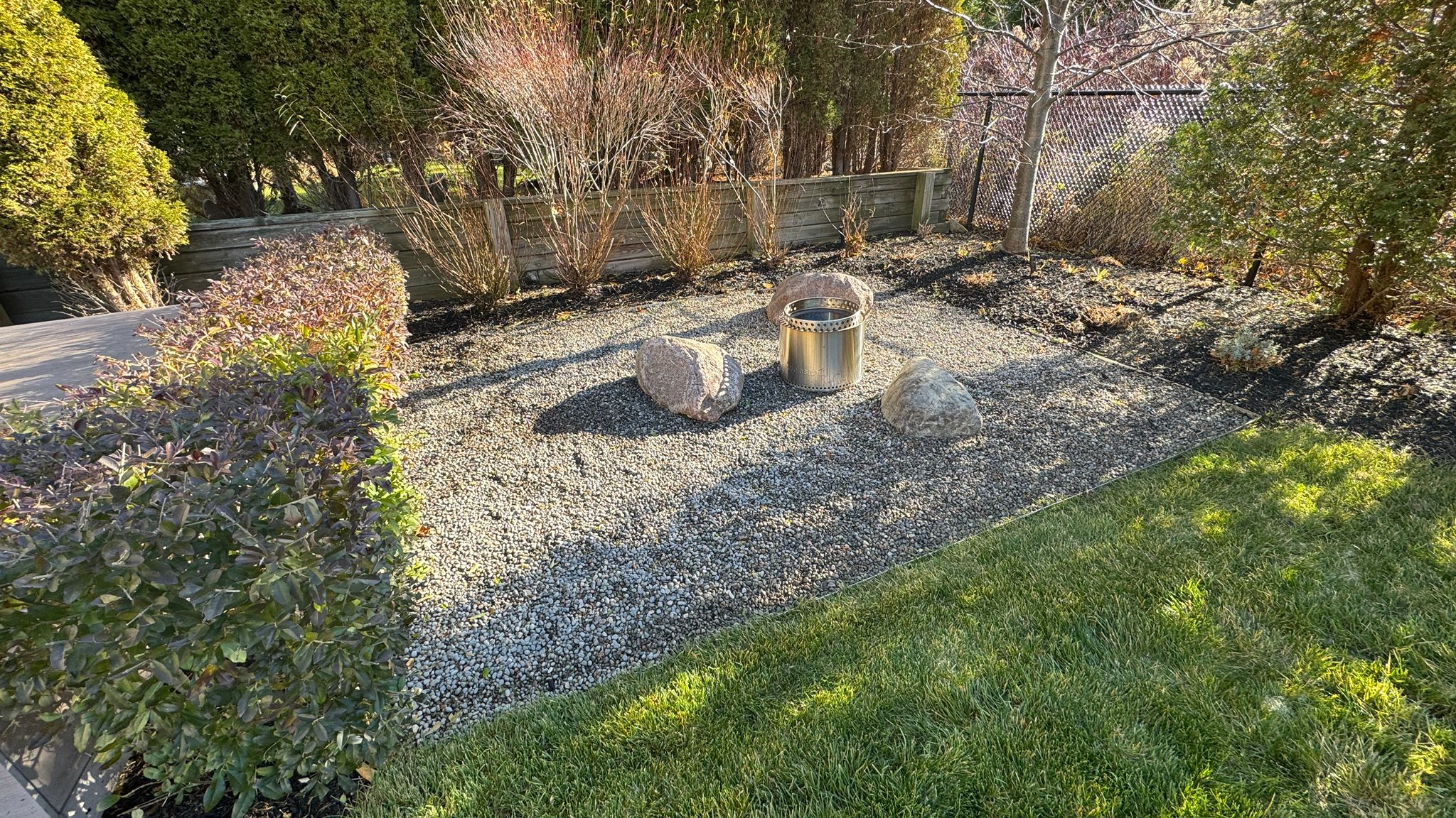 Backyard fire pit surrounded by stones and greenery.