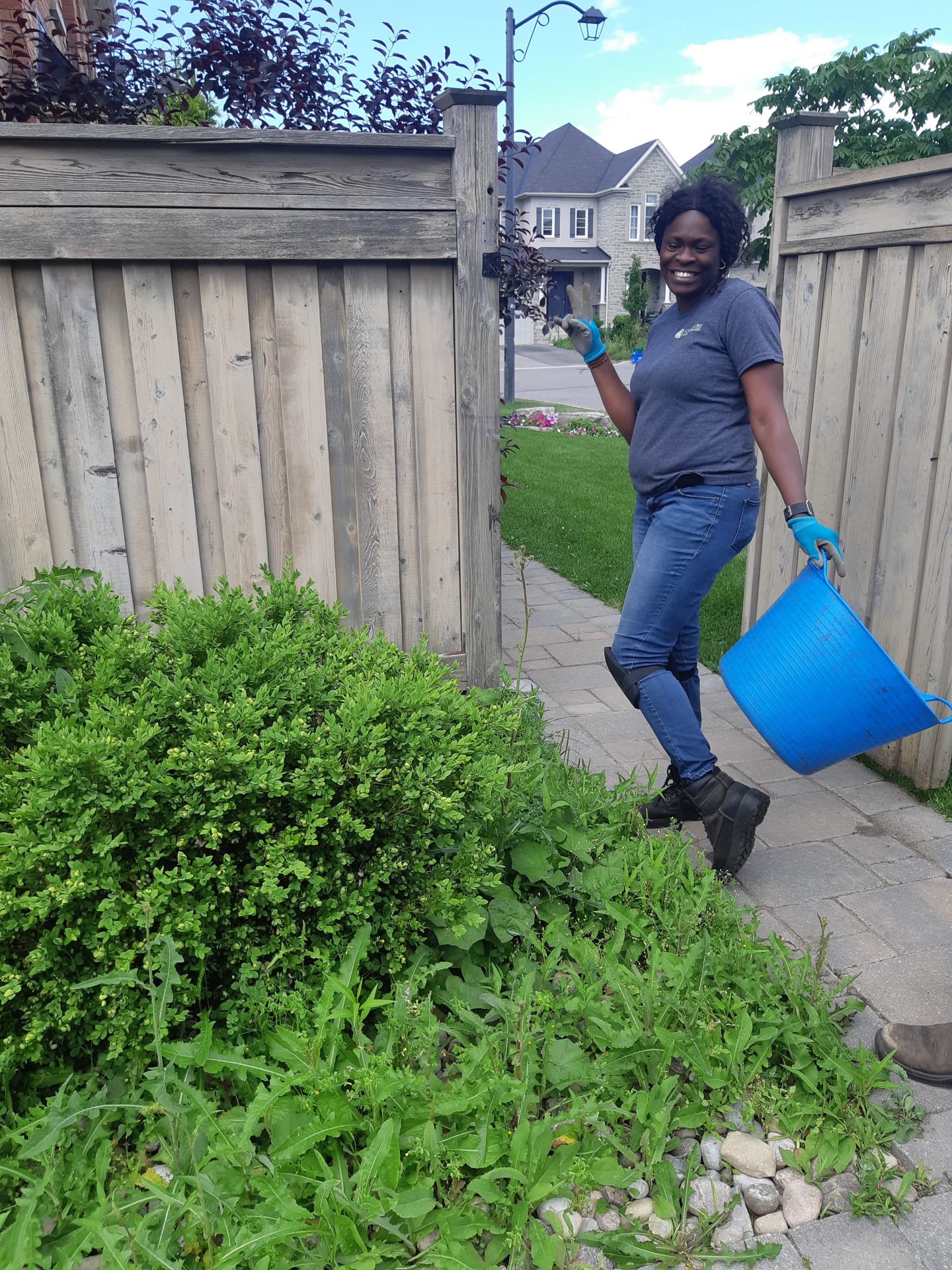 Person gardening with blue bucket, smiling outdoors.