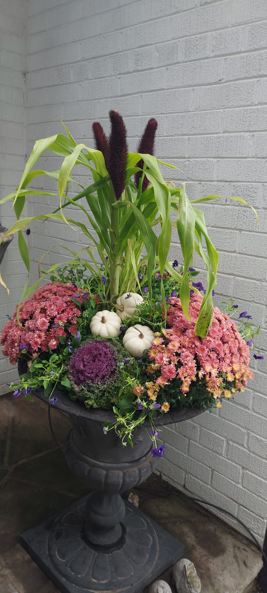Autumn floral arrangement with pumpkins and corn stalks.